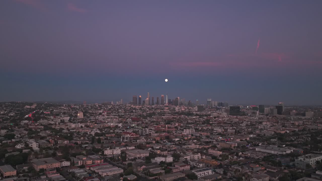 Aerial wide flyover shot of a full moon over the downtown skyline at blue hour in Los Angeles, California. 4K