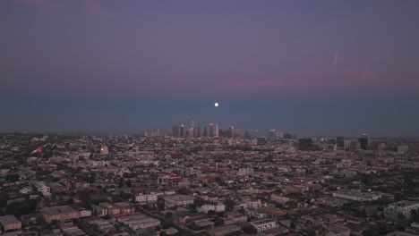 aerial wide flyover shot of a full moon over the downtown skyline at blue hour in los angeles, california. 4k