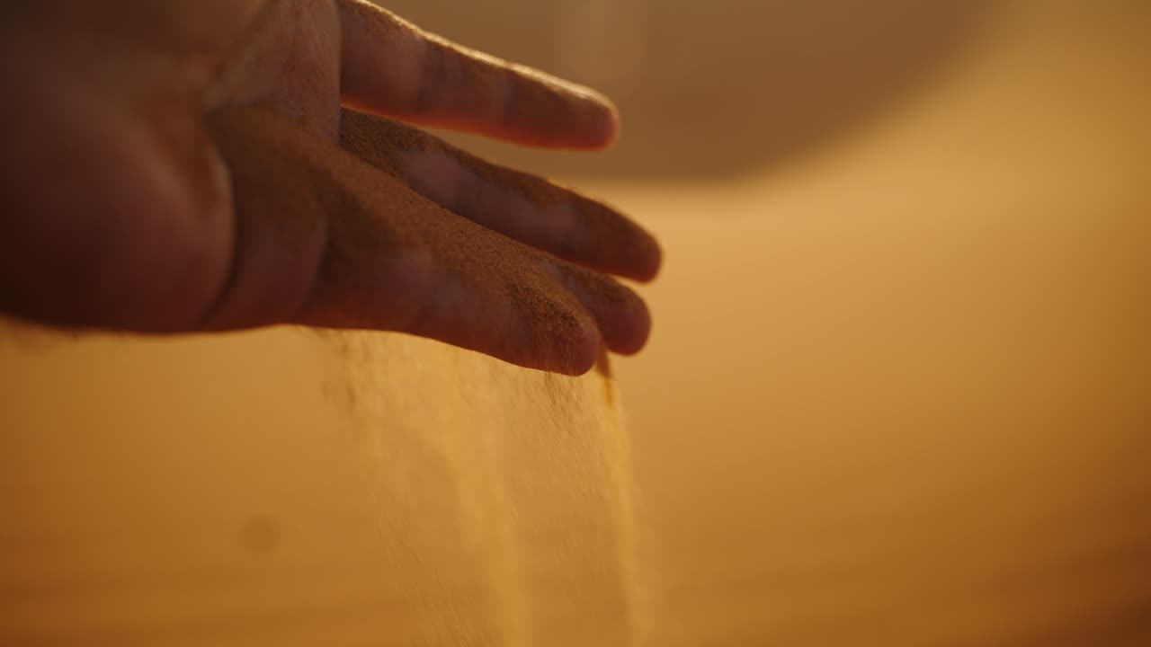 Close-up of golden desert sand slipping gracefully through a hand at sunset in the Sahara Desert, Morocco, with warm light creating a soft glow
