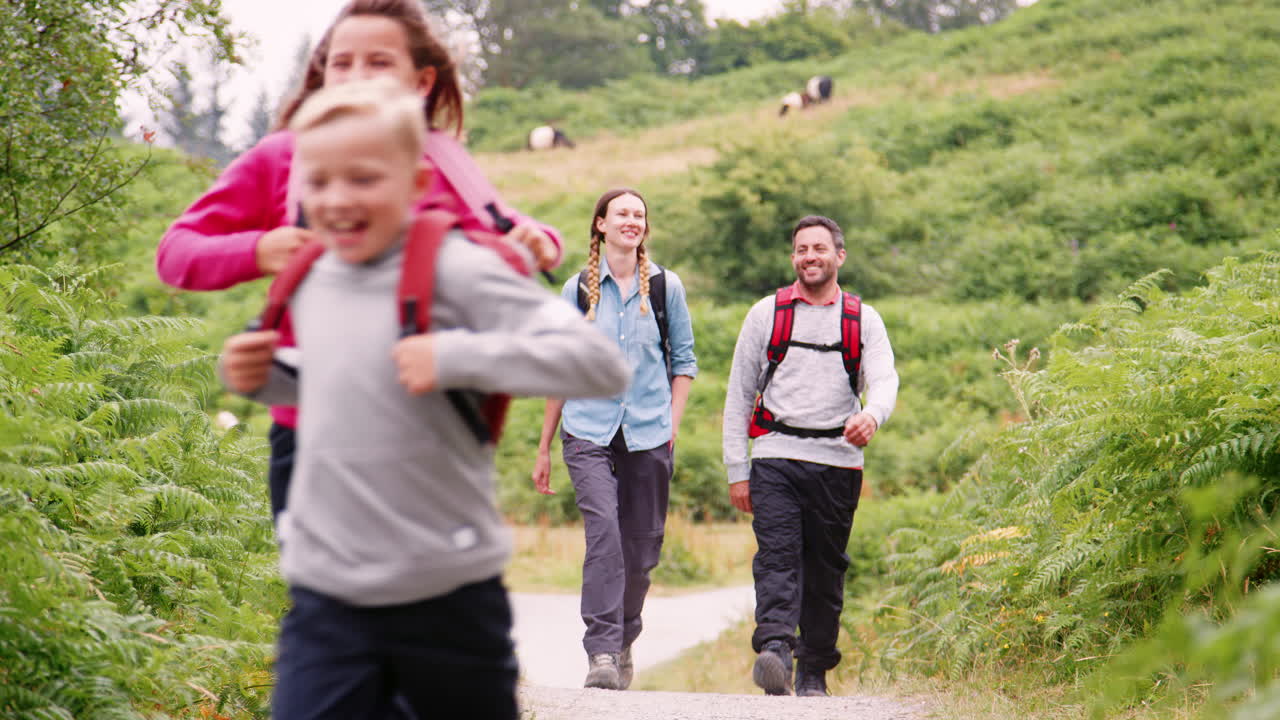 niños corriendo delante de sus padres caminando por un sendero rural durante un viaje de campamento familiar, lake district, reino unido