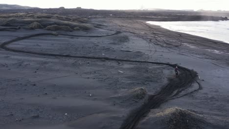 person on motorbike driving on black sand beach in iceland, sunrise