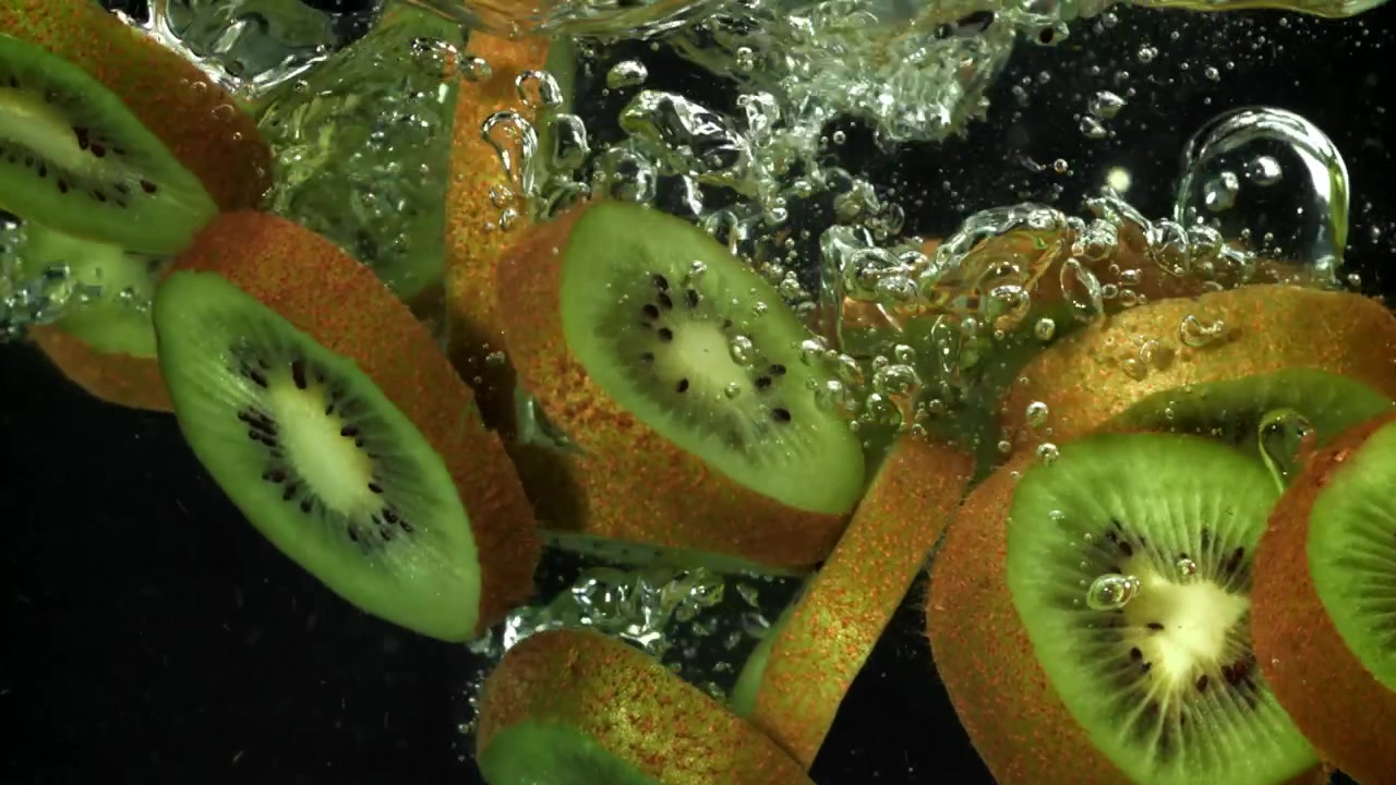 Fresh Kiwi Slices Falling into Water with Bubbles on Black Background