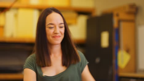 Una-Mujer-Joven-Sonríe-Orgullosamente-En-Un-Taller-Industrial-Después-De-Colocar-Una-Tabla-De-Dos-Por-Cuatro-Ensamblando-A-Mano-Un-Armazón-De-Cama-De-Madera.