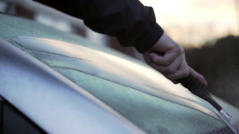 using an ice scrapper to remove ice from a car windscreen on a cold winter morning