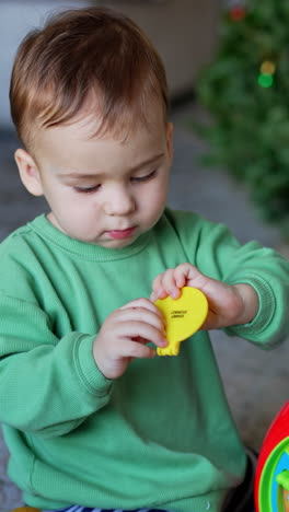 cute child holds a part from toy surprised that it fell off. adorable boy continues his game pressing buttons on a toy. christmas tree. vertical video