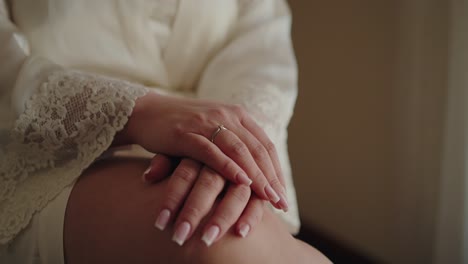 close up of a bride’s hands with a gold ring resting on her lap in soft lighting