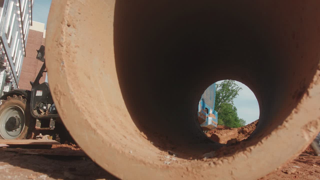 A construction worker passes across a job site and is visible through a concrete tube