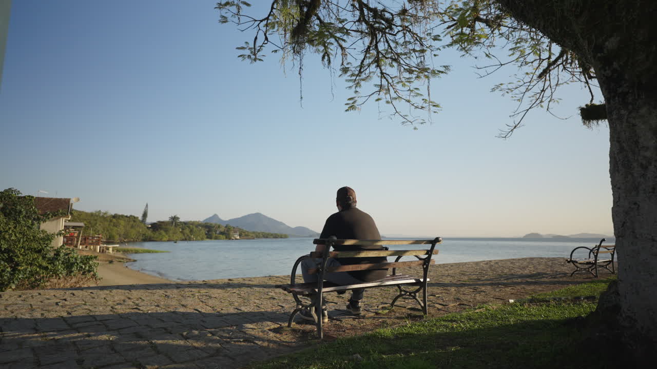 Lonely man sitting on a bench by the sea, gazing at the calm coastal landscape