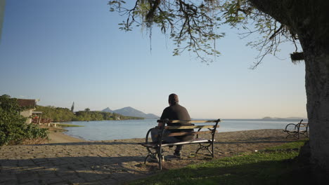 lonely man sitting on a bench by the sea, gazing at the calm coastal landscape