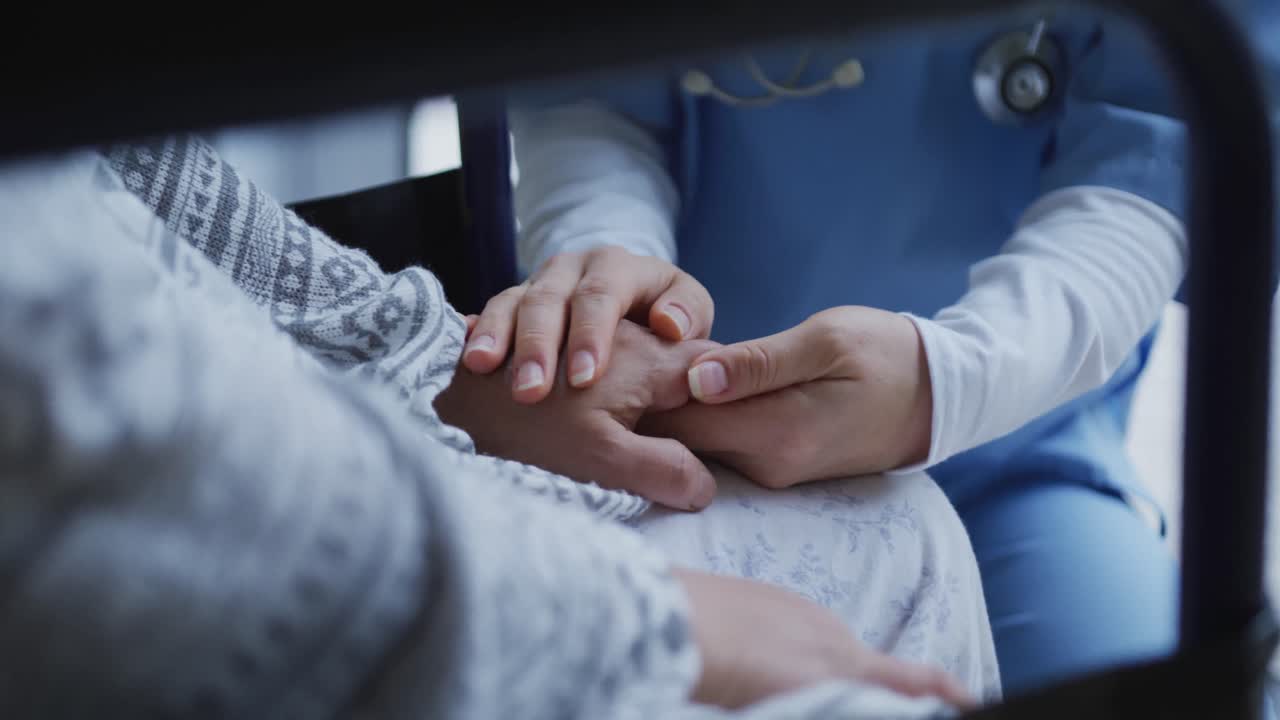 sección media de una doctora asiática que sostiene las manos de una paciente y la consuela en el hospital