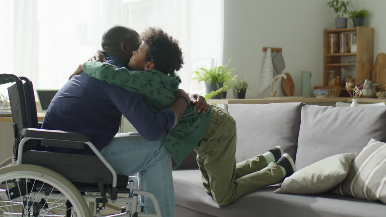 Man in Wheelchair Hugging Little Son at Home