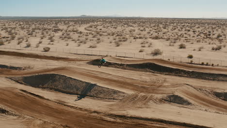 Bandeja-De-Seguimiento-Aéreo,-Piloto-De-Motocross-Saltando-Y-Tomando-Aire-En-El-Circuito-Del-Desierto