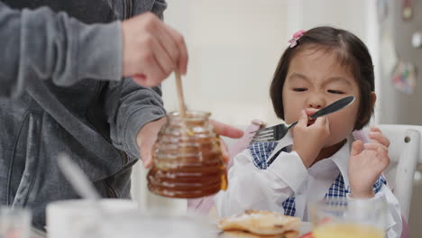 귀여운 작은 아시아 소녀가 아침 식사를 하고 있다. 아버지는 딸을 위해 와플을 준비하고 있다. 집에서 부 ⁇ 에서 맛있는 집에서 만든 식사를 즐기고 있다. 학교에 갈 준비를 하고 있다.