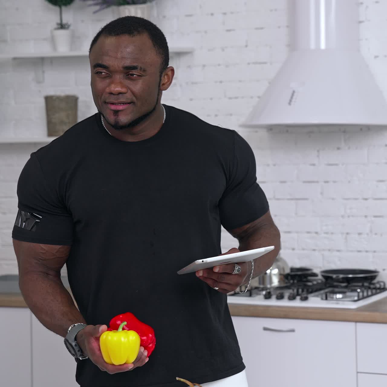 Sportivo afroamericano in cucina. Ritratto di un uomo di colore pensieroso con corpo muscoloso che tiene in mano un tablet e verdure fresche biologiche