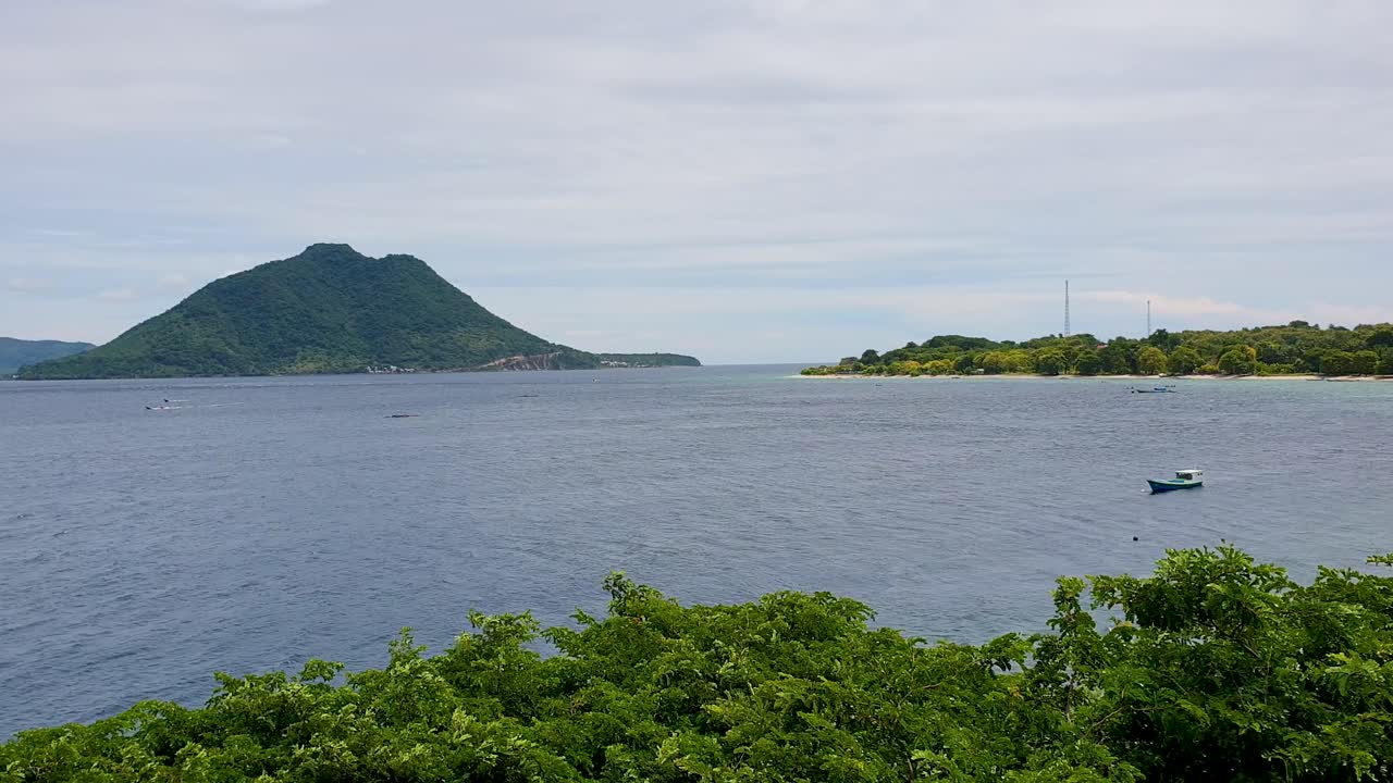 Scenic view overlooking ocean with small fishing boat and volcanic tropical island on Alor Island in Lesser Sunda Islands of East Nusa Tenggara, Indonesia