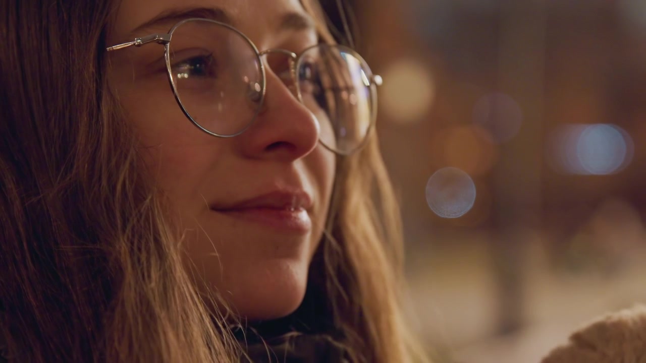 White woman with glasses cuddling teddy on bench closeup nighttime city portrait with warm bokeh lights, soft coat and scarf, gentle smile and tearful gaze, tender touch on plush toy, cinematic