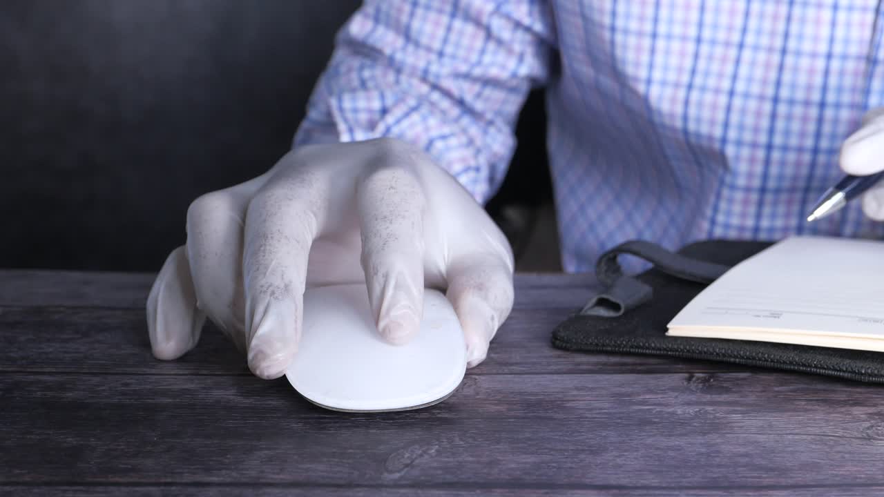Person in gloves working at a computer desk with notebook and pen