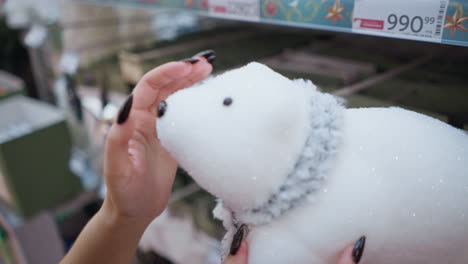 close-up of a hand with black polished nails affectionately touching a plush polar bear, emphasizing its texture against a blurred background