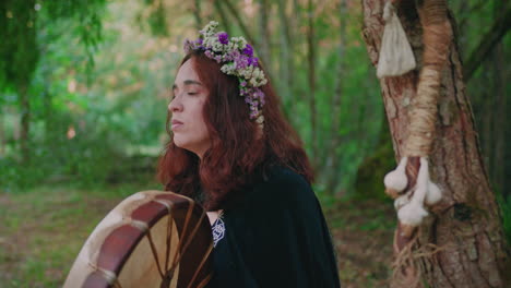 druid girl in a forest playing a shamanic drum side view medium shot