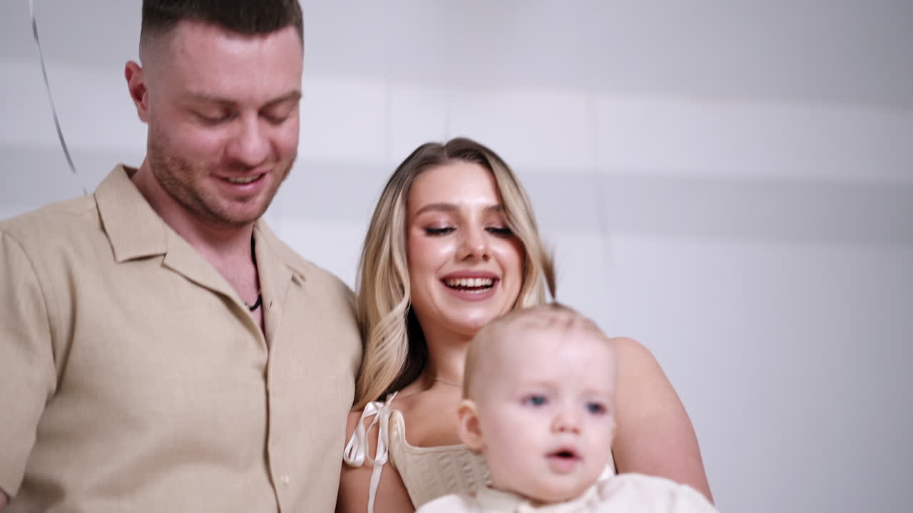 Smiling blond woman tossing a little baby in hands. Happy parents with their infant child. Family portrait.