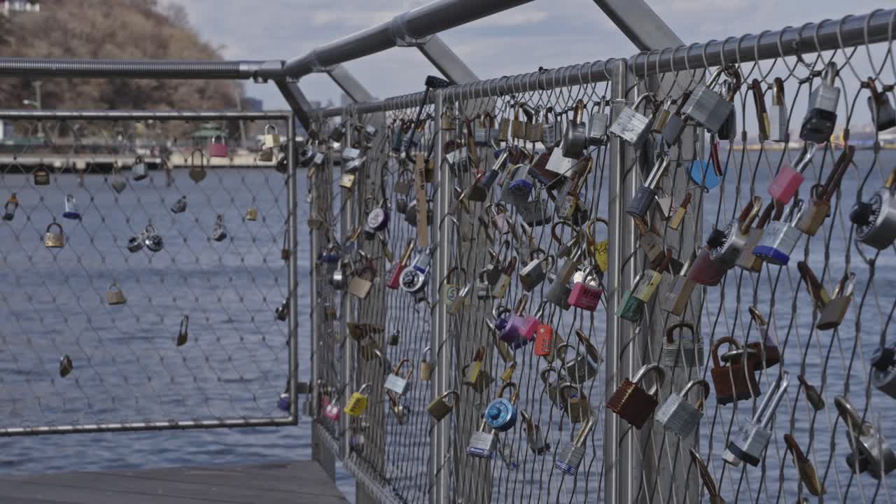 A collection of colorful padlocks fastened to a waterfront fence, symbolizing love and commitment against the backdrop of calm waters