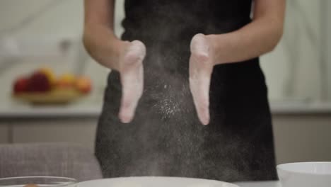 professional female cook claps her hands and powder flies. concept: the production of sweets bread dough. ingredients and preparation stages. slowmotion