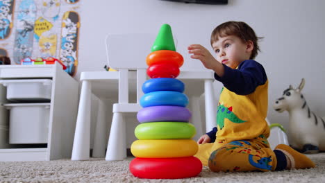 adorable two-year old toddler building a pyramid at home. baby boy sits on the floor busy with his game. low angle view.