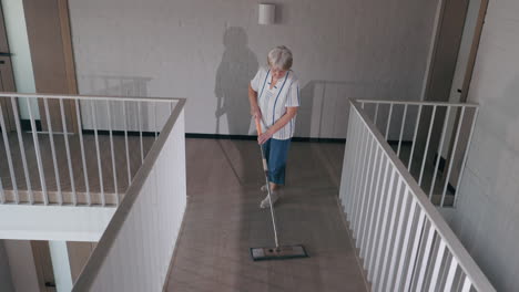 elderly woman mopping a hallway floor