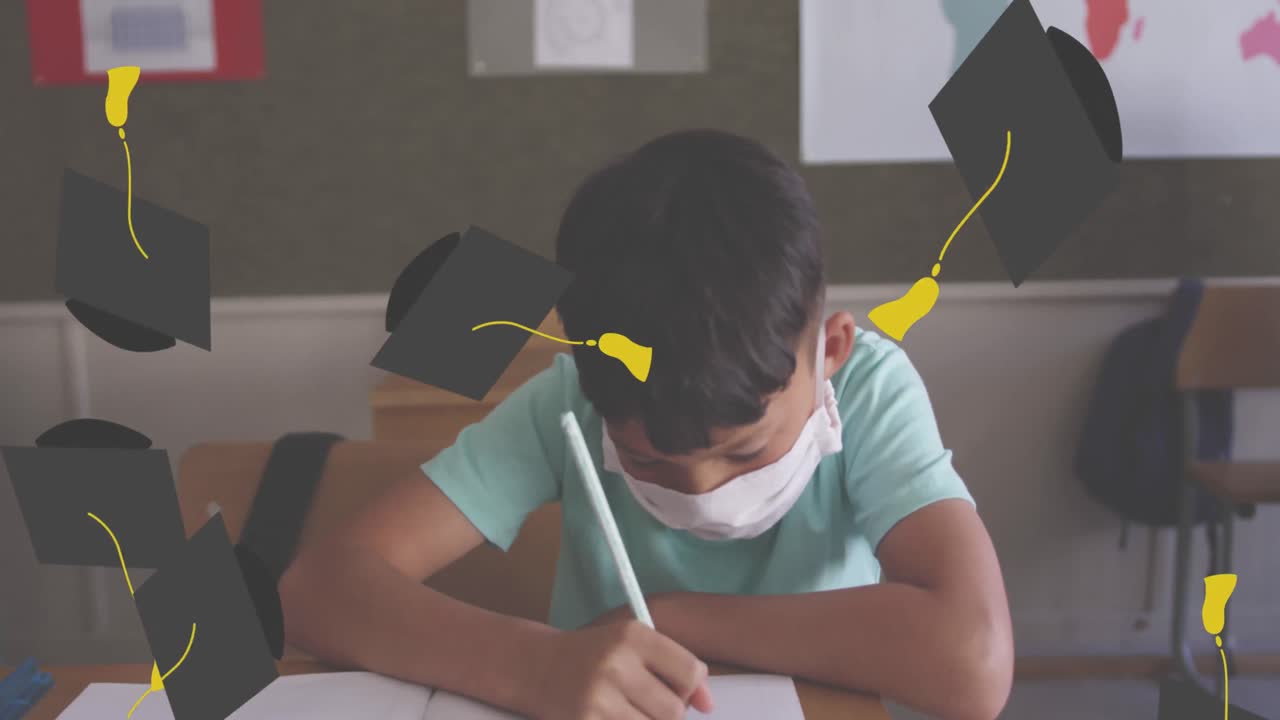 Animation of falling academic cap over boy wearing face mask sitting in classroom writing