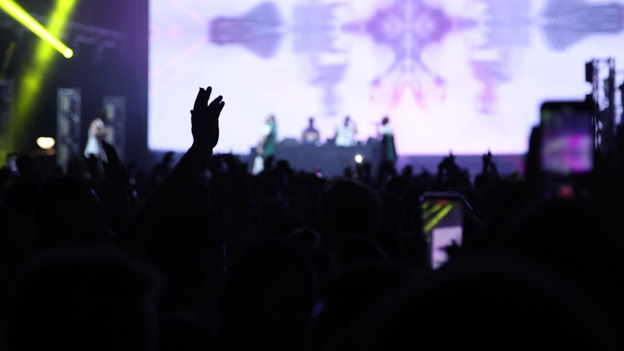 Animazione colorata sul palco di un concerto notturno con fuoco e fumo e persone entusiaste che applaudono, ripreso al rallentatore