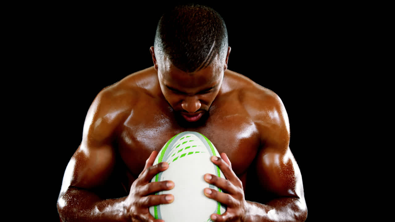 Giocatore di rugby professionista che tiene in mano un pallone su sfondo nero