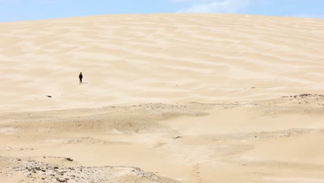 a young boy walks off into the distance of a big sand dune in australia
