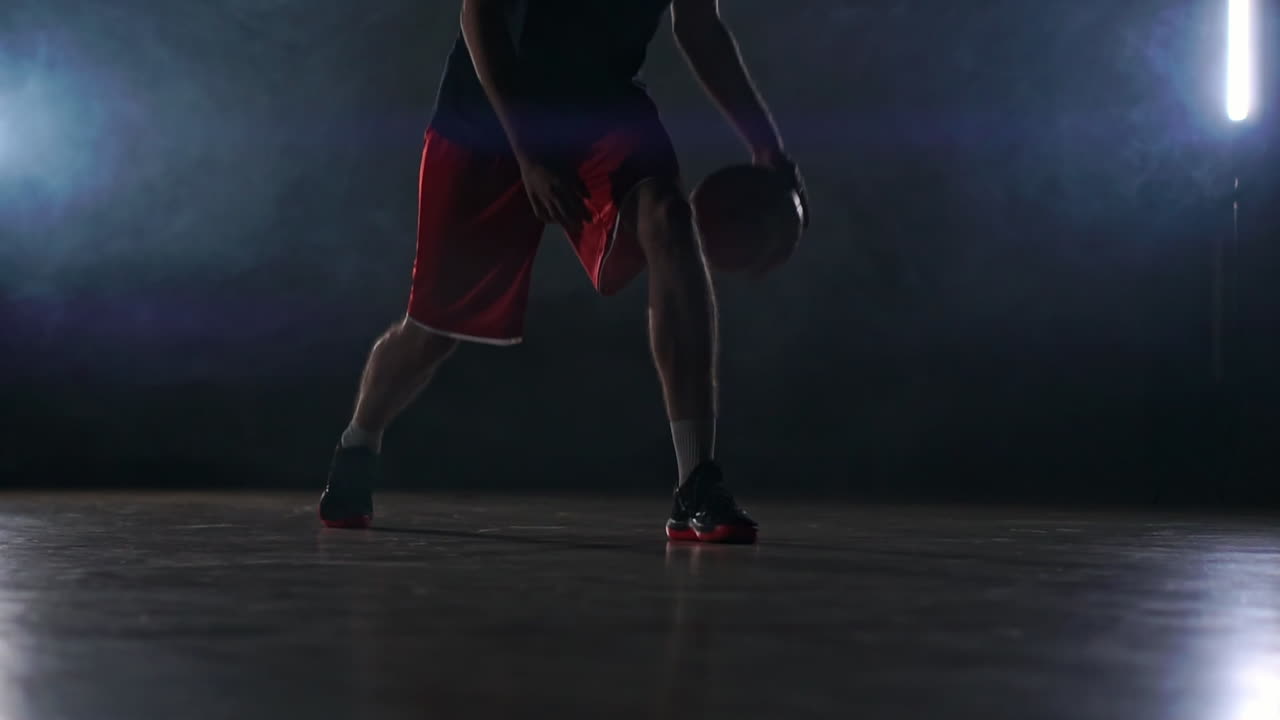 one young adult man, basketball player dribble ball, dark indoors basketball court smoke. Slow motion