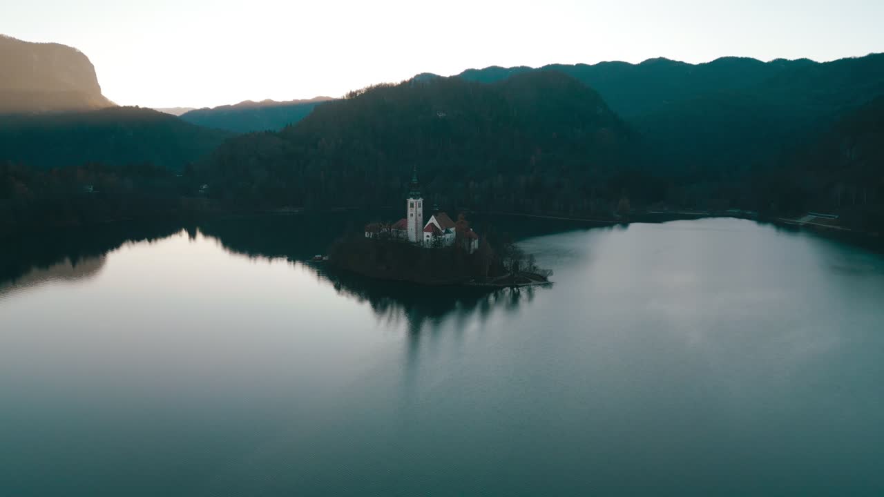 Dall'alto, le acque tranquille si dividono intorno alla piccola isola della chiesa mentre il filmato avanza lentamente verso il luogo simbolo nel Lago di Bled, Slovenia.