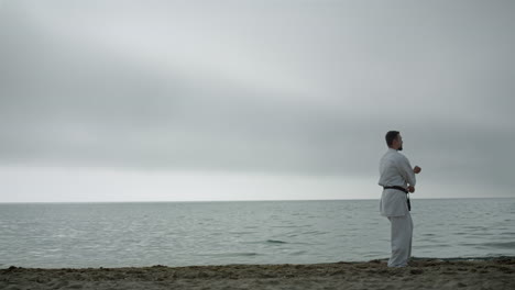 fit athlete workout kungfu on sandy beach. man exercising combat technique.