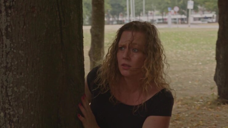 Scared woman running through a park while being chased by two people in the background