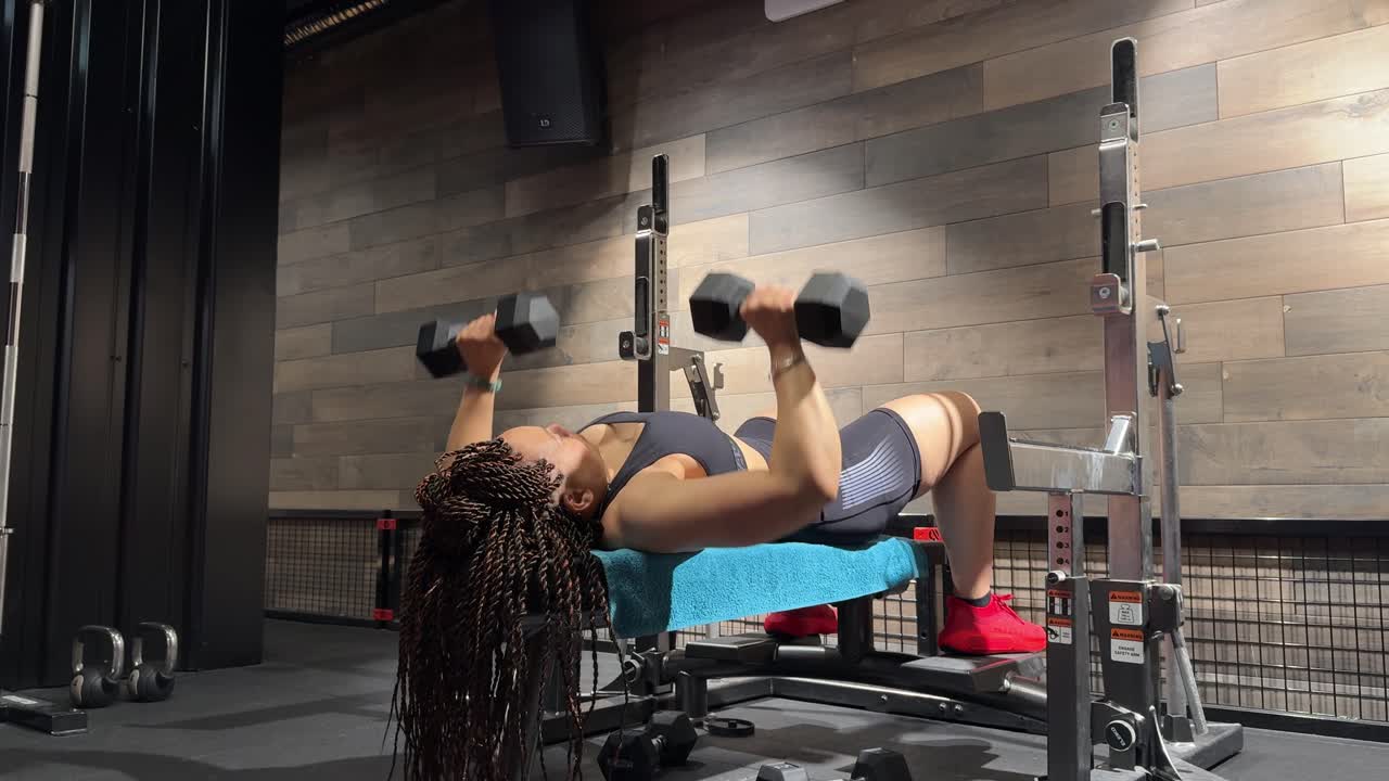 A woman lies on a bench and performs multiple dumbbell chest presses, lifting and lowering the weights over her face