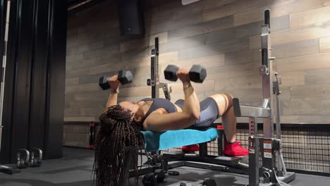 a woman lies on a bench and performs multiple dumbbell chest presses, lifting and lowering the weights over her face
