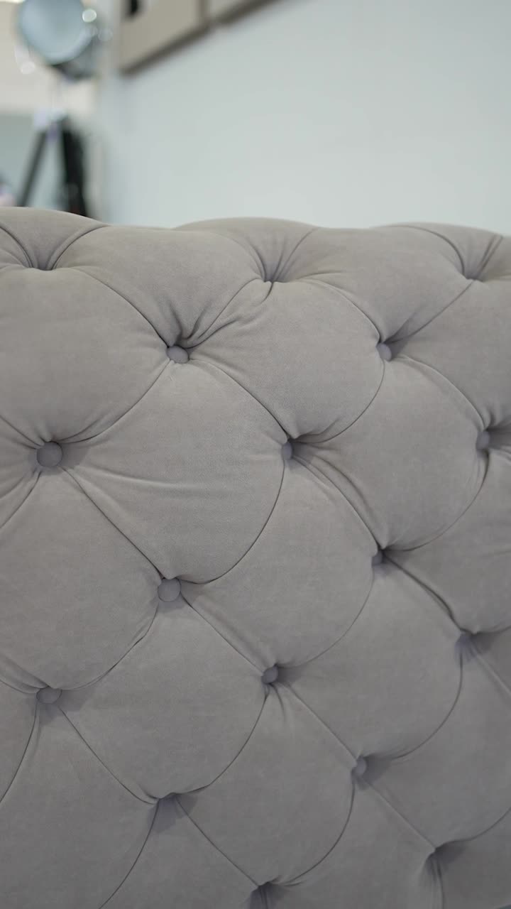 This close-up view highlights the soft gray tufted upholstery of a chair or couch in a well-designed interior. The craftsmanship and style emphasize comfort and elegance