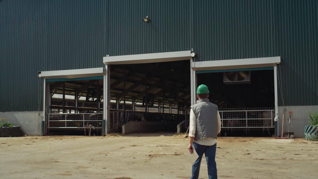 trabajador caminando en una instalación de ganadería que tiene un clipboard. industria de productos lácteos.