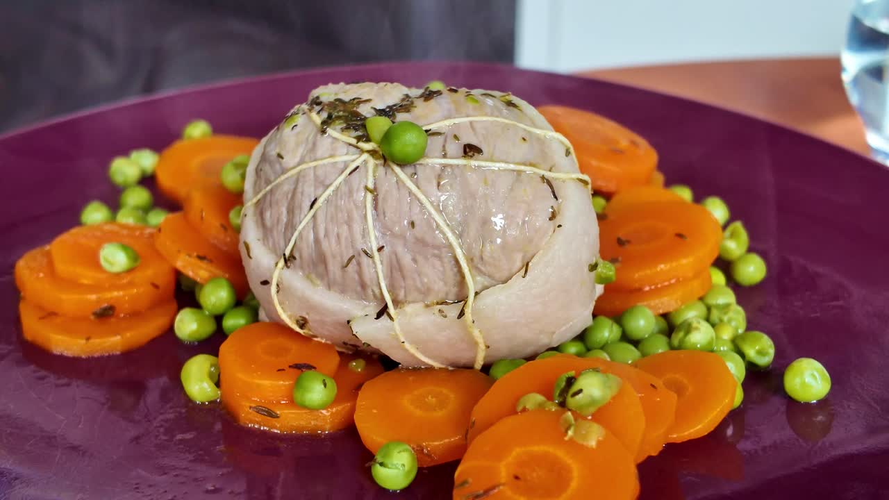 Orbiting close-up of a steaming meat dish with carrots and peas on a purple plate