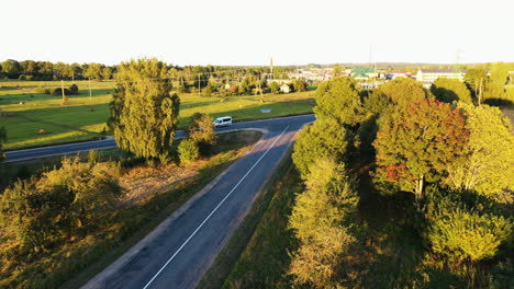Asphalt-road-in-rural-area-with-small-town-in-background,-sunny-dusk-time,-aerial-view
