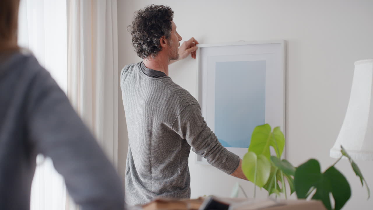 pareja feliz mudándose a una nueva casa colgando fotos en la pared decorando la casa disfrutando del trabajo en equipo 4k