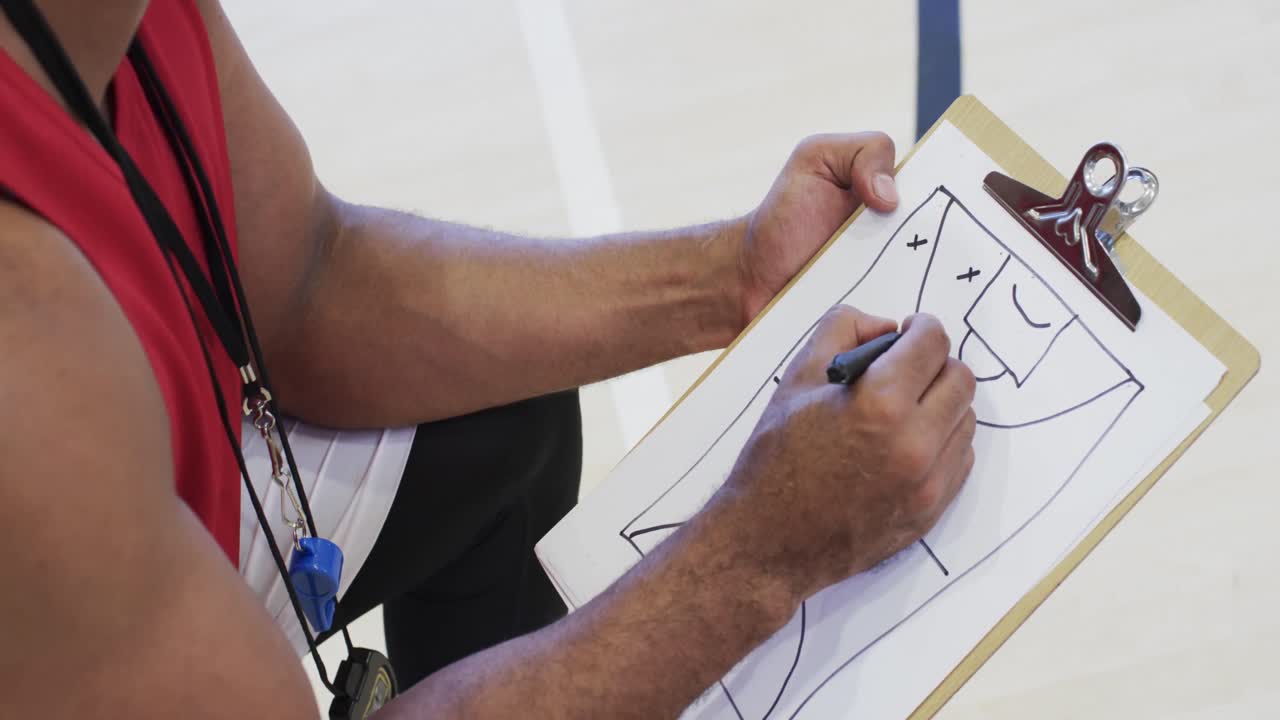 entrenador de baloncesto afroamericano usando un cuaderno en una cancha cubierta, en cámara lenta
