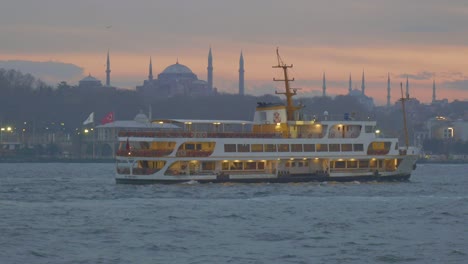 ferry boat sailing past the hagia sophia and blue mosque in istanbul, turkey at sunset