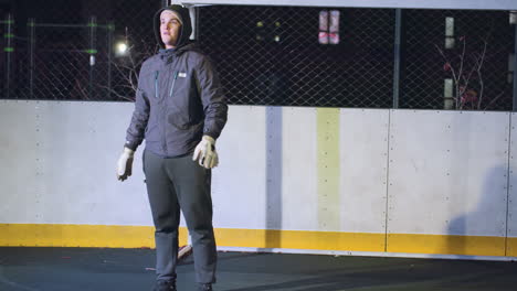 goalkeeper kicks soccer ball into field with precision and focus during night training on urban outdoor sports court, background includes metallic fence and illuminated residential buildings