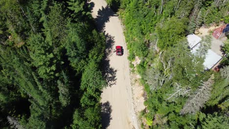 rising aerial shot of red vehicle on dirt road surrounded by green forest on hot summer day