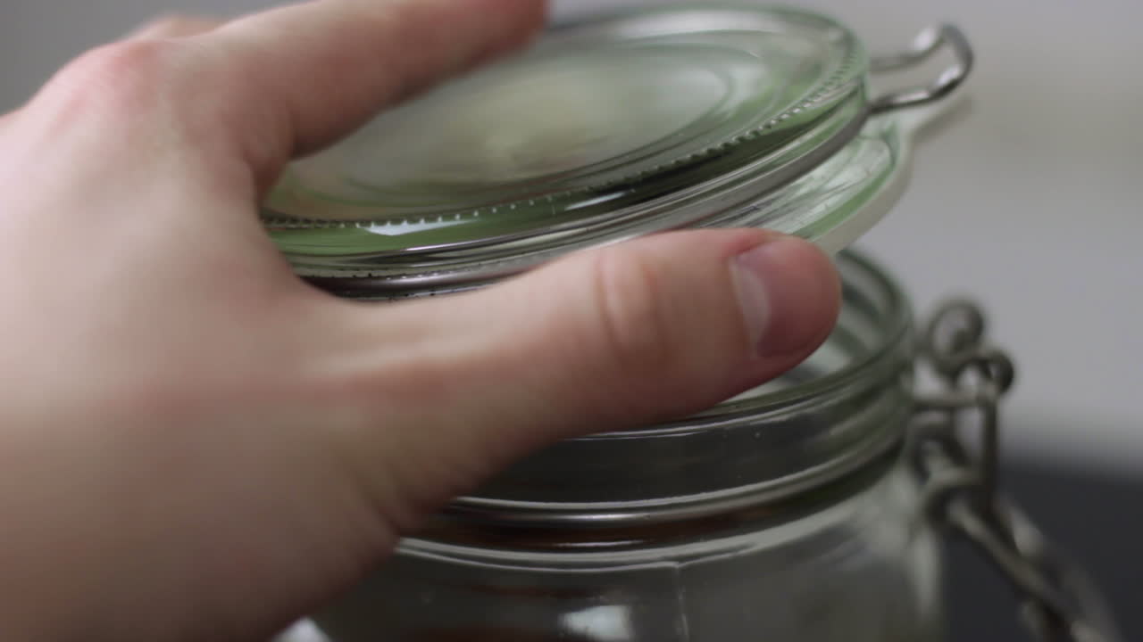 Close up of opening the clasp on a glass mason jar and lifting the lid before tilting the jar forwards