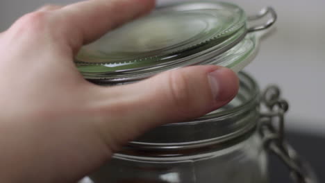 close up of opening the clasp on a glass mason jar and lifting the lid before tilting the jar forwards