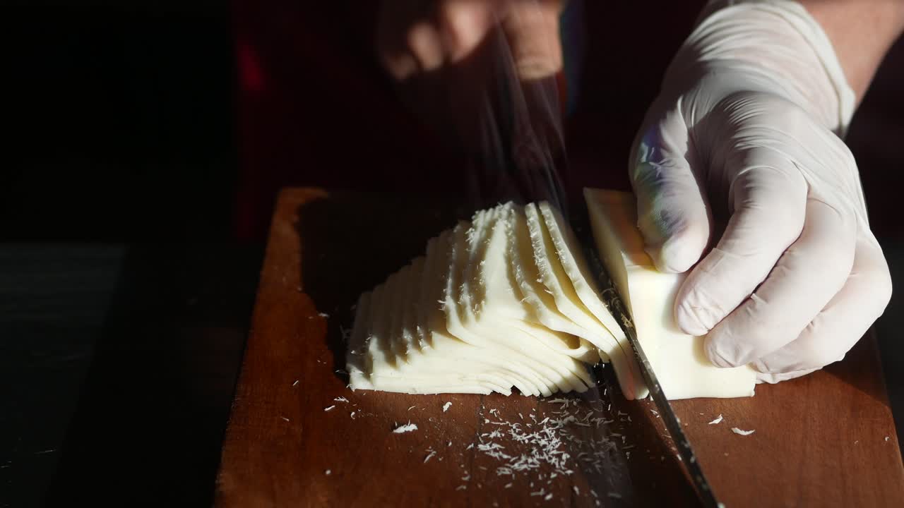 Close-up of a person in gloves slicing cheese on a cutting board